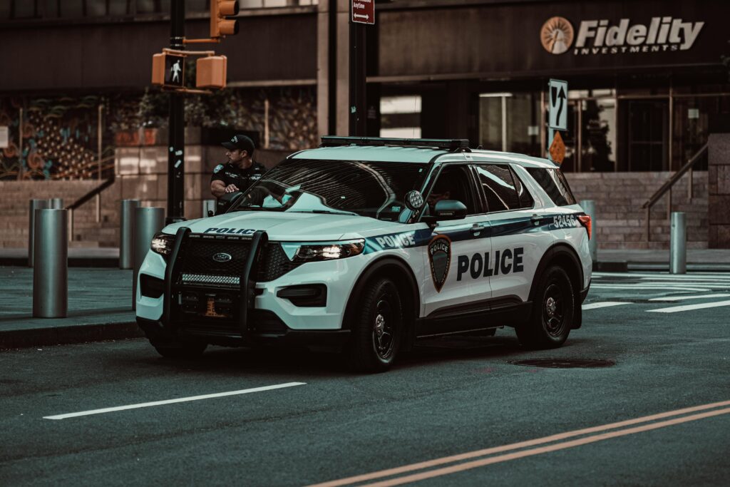 A police car parked on a street in New York City with a policeman nearby, showcasing urban safety.