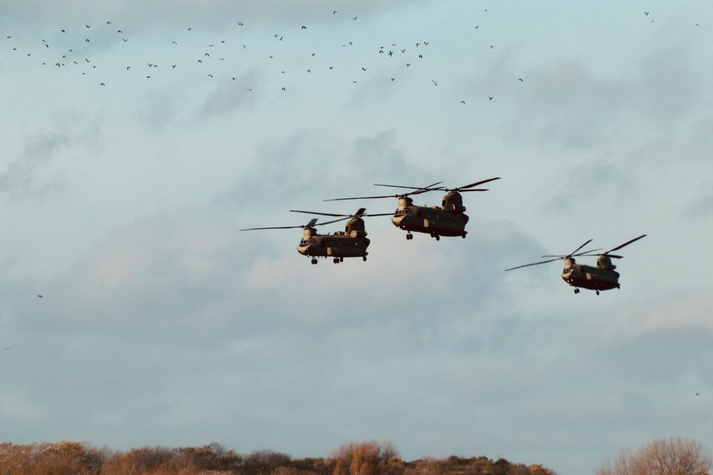 Three Chinook helicopters flying in formation against a cloudy sky, creating a dramatic silhouette.