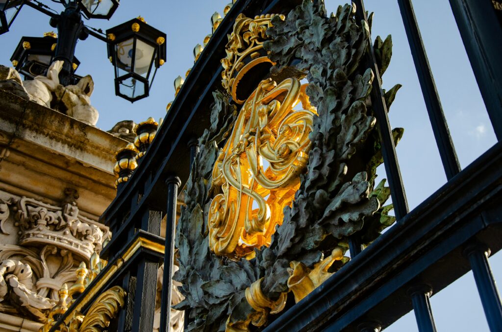 Close-up of gilded ironwork at Buckingham Palace gates in London, showcasing intricate design.