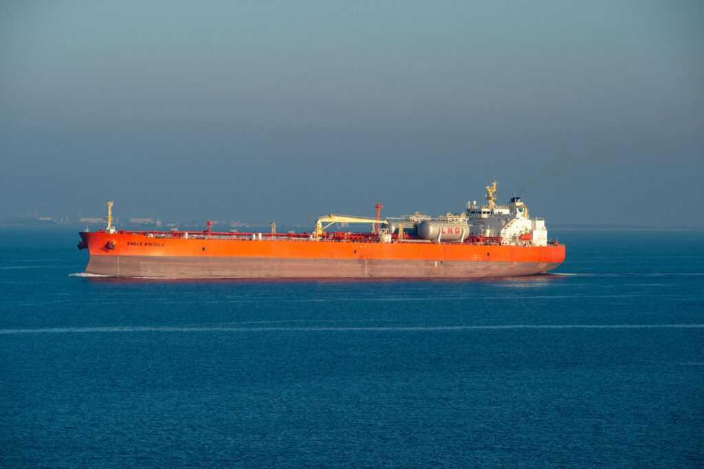 Bright orange LNG carrier ship cruising through calm sea waters on a clear day.