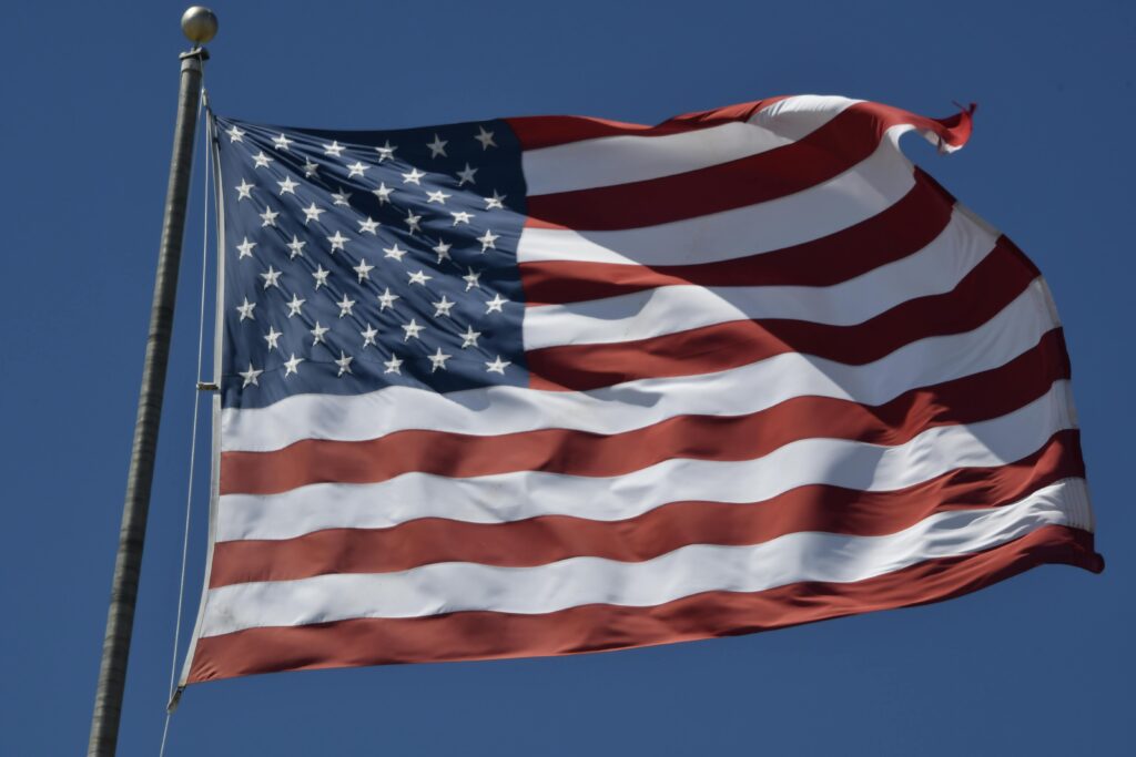 pexels-photo-33616820-33616820 United States flag waving prominently against a clear, bright blue sky, symbolizing patriotism and freedom.