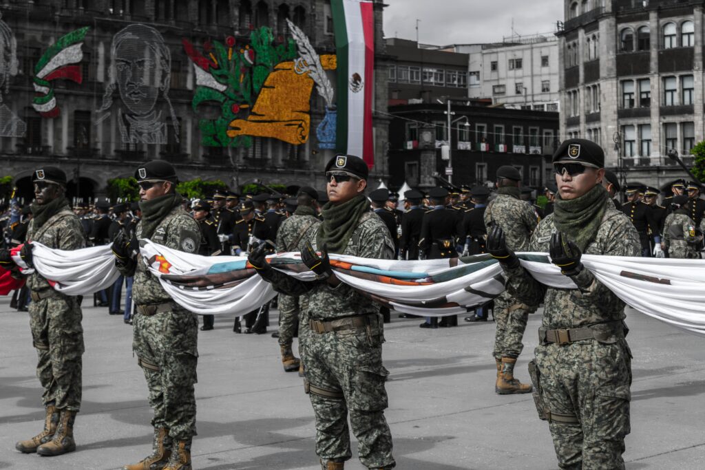Soldiers in camouflage uniforms hold a flag during a parade in Zócalo, Mexico City.