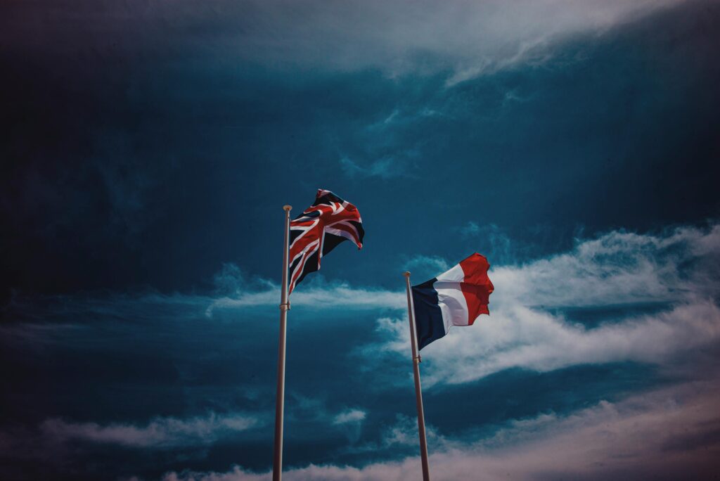 From below of flags of United Kingdom and France waving against cloudy blue sky