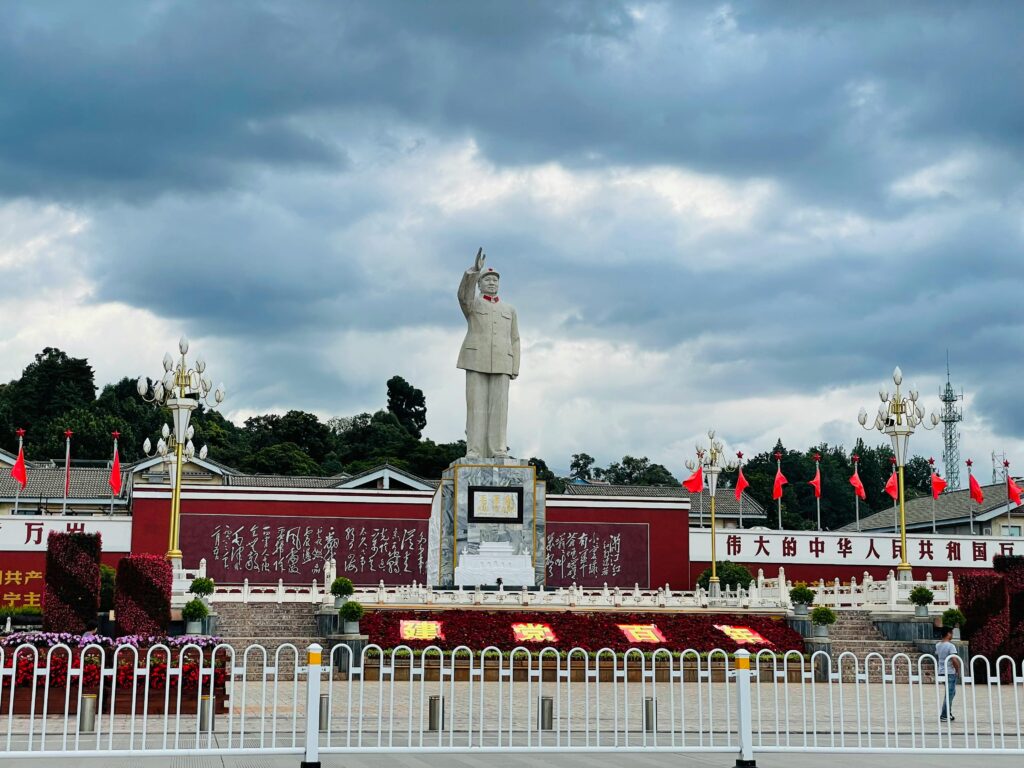 Statue of Mao Zedong in a public plaza with red flags and Chinese inscriptions.